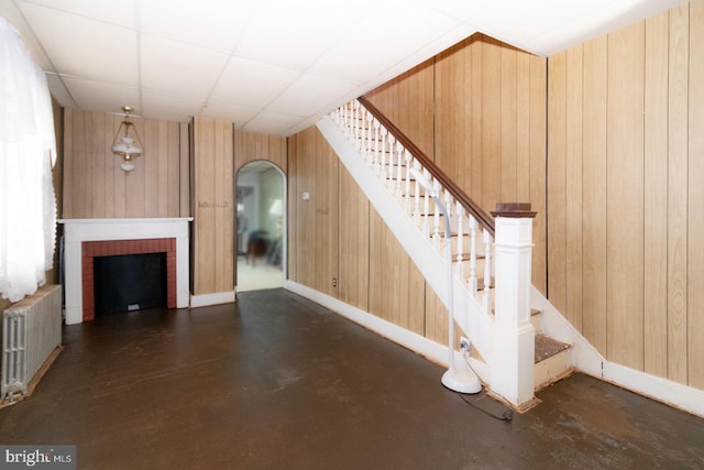 interior space featuring wooden walls, arched walkways, radiator, a paneled ceiling, and a brick fireplace