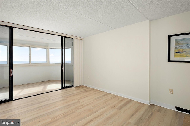 unfurnished room featuring light wood-style floors, baseboards, and a textured ceiling