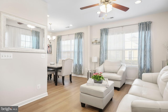 living area with visible vents, ceiling fan with notable chandelier, light wood-type flooring, and baseboards