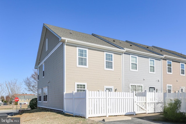 rear view of house with a gate, a shingled roof, and fence