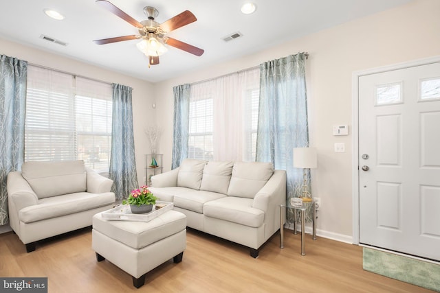 living room featuring ceiling fan, visible vents, baseboards, and light wood-style flooring