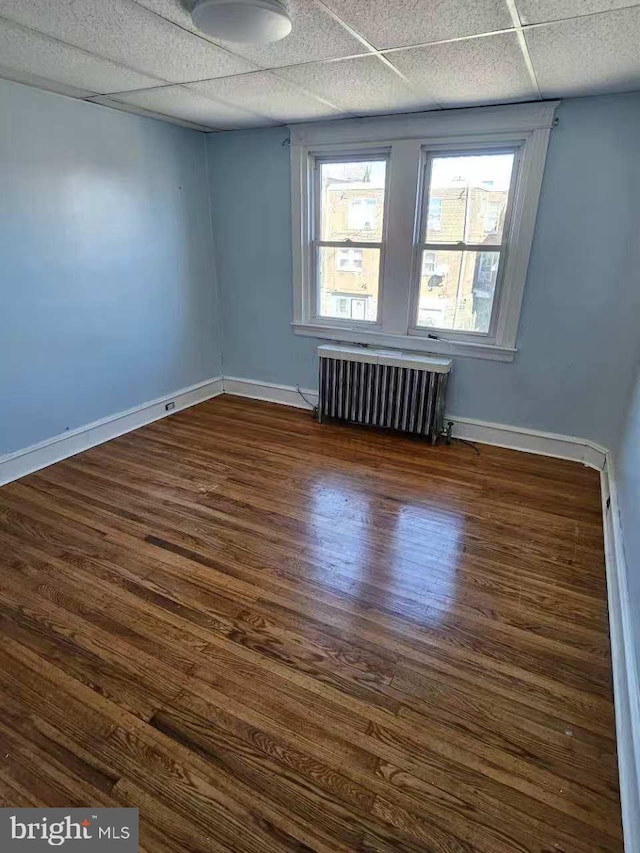 empty room with a paneled ceiling, baseboards, radiator heating unit, and wood finished floors