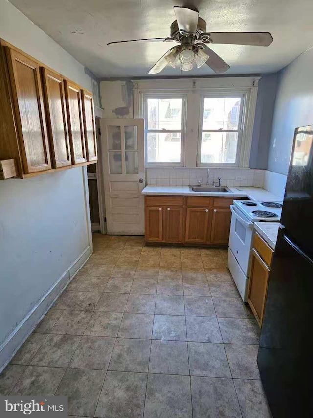 kitchen featuring brown cabinets, light tile patterned floors, white range with electric cooktop, freestanding refrigerator, and a sink