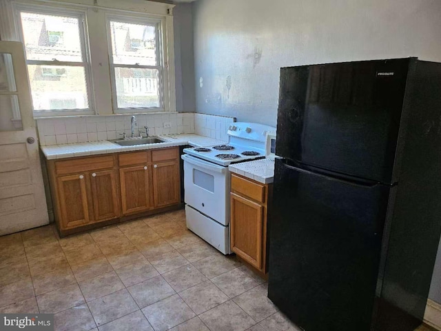 kitchen with a sink, electric stove, brown cabinets, tile counters, and freestanding refrigerator