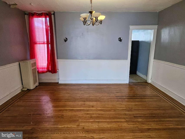 unfurnished dining area featuring a chandelier, radiator heating unit, wood finished floors, and a wainscoted wall