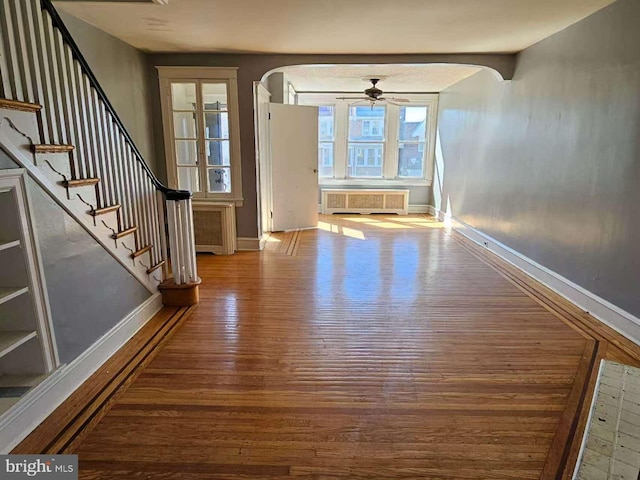 foyer featuring arched walkways, baseboards, wood finished floors, and radiator