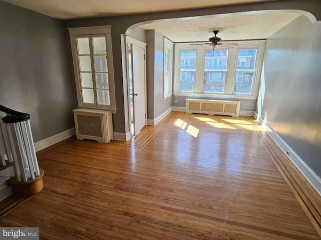 interior space featuring arched walkways, radiator heating unit, and wood finished floors