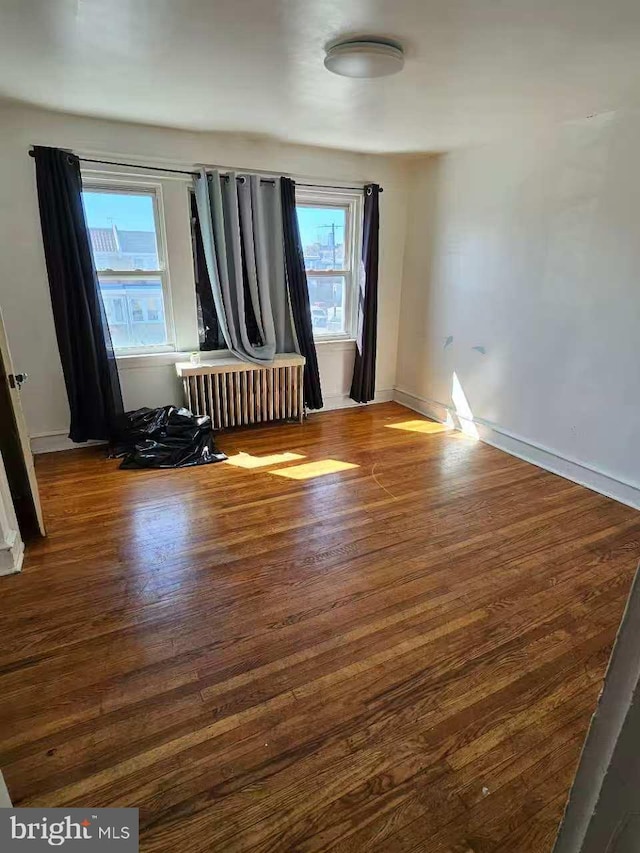 spare room featuring radiator, baseboards, and wood finished floors