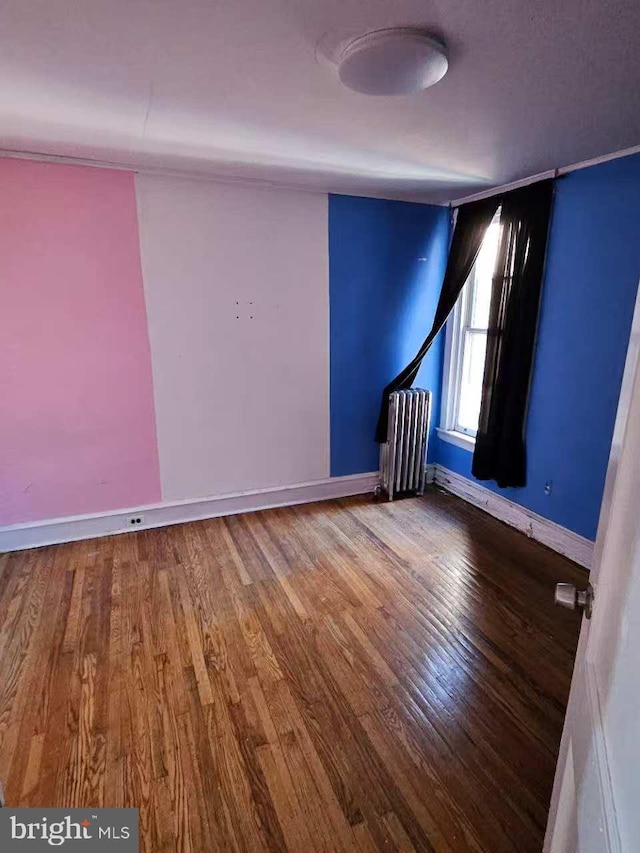 unfurnished room featuring baseboards, radiator heating unit, and wood finished floors