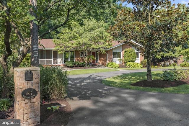 ranch-style home featuring driveway, brick siding, a front lawn, and a sunroom