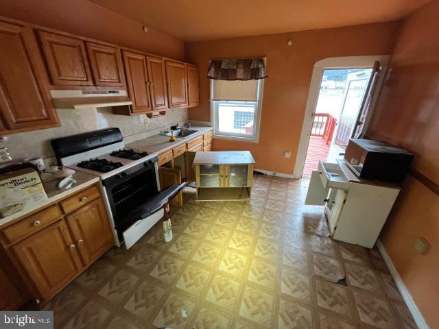 kitchen with brown cabinets, white gas stove, light countertops, under cabinet range hood, and baseboards