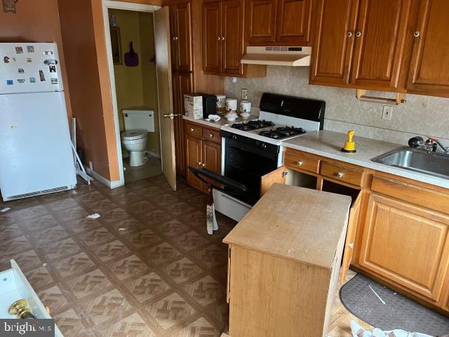 kitchen featuring gas range oven, light countertops, freestanding refrigerator, a sink, and under cabinet range hood