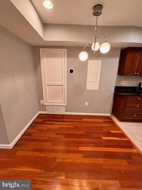 unfurnished dining area featuring light wood finished floors, electric panel, and baseboards