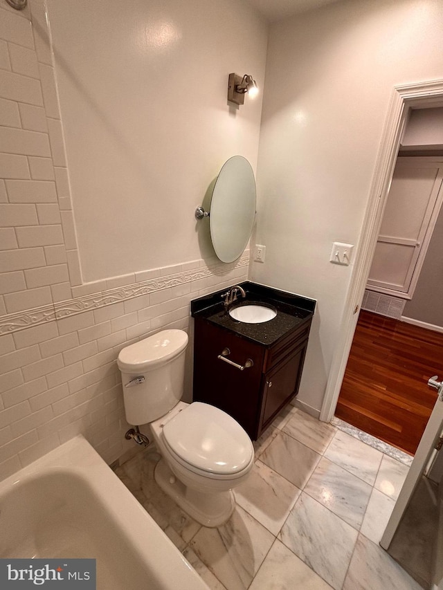 bathroom featuring toilet, a bathing tub, vanity, tile walls, and marble finish floor