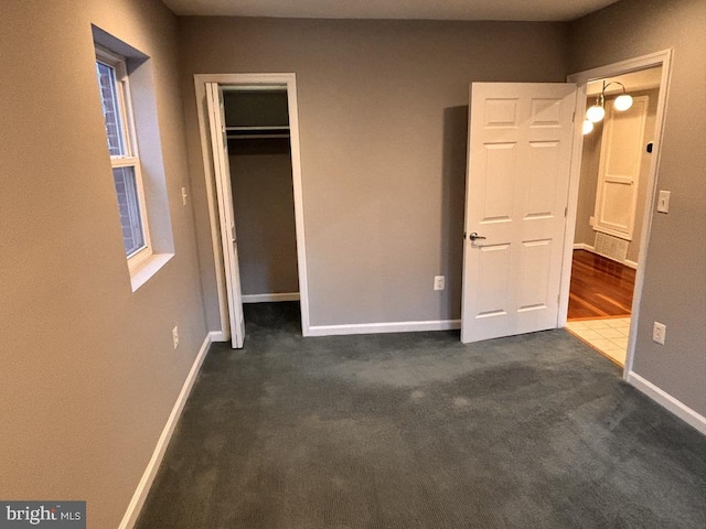 unfurnished bedroom featuring dark colored carpet, a closet, and baseboards