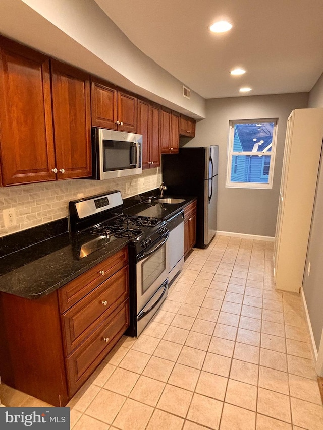 kitchen featuring light tile patterned floors, baseboards, brown cabinetry, appliances with stainless steel finishes, and backsplash