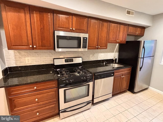 kitchen with stainless steel appliances, visible vents, backsplash, a sink, and dark stone countertops