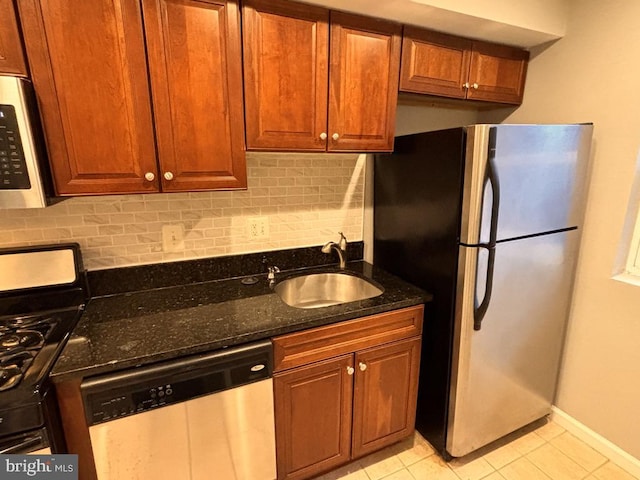 kitchen with light tile patterned floors, stainless steel appliances, a sink, tasteful backsplash, and dark stone countertops