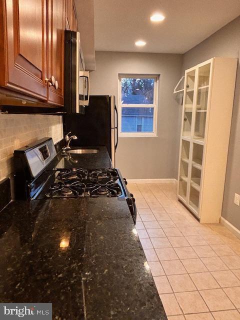 kitchen featuring light tile patterned floors, tasteful backsplash, dark stone counters, stainless steel appliances, and a sink