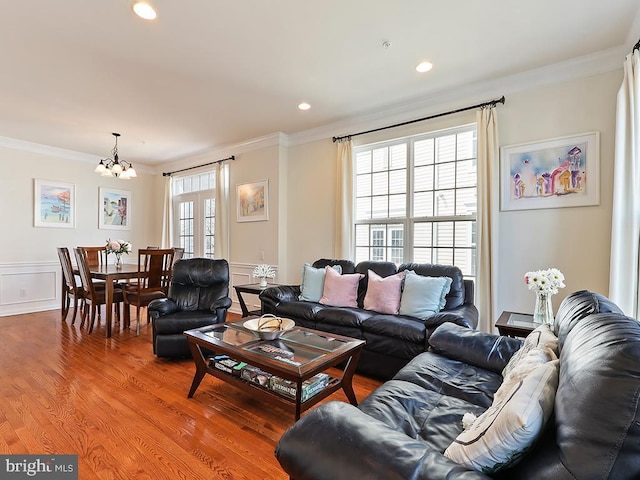 living area with light wood-type flooring, a notable chandelier, crown molding, and wainscoting