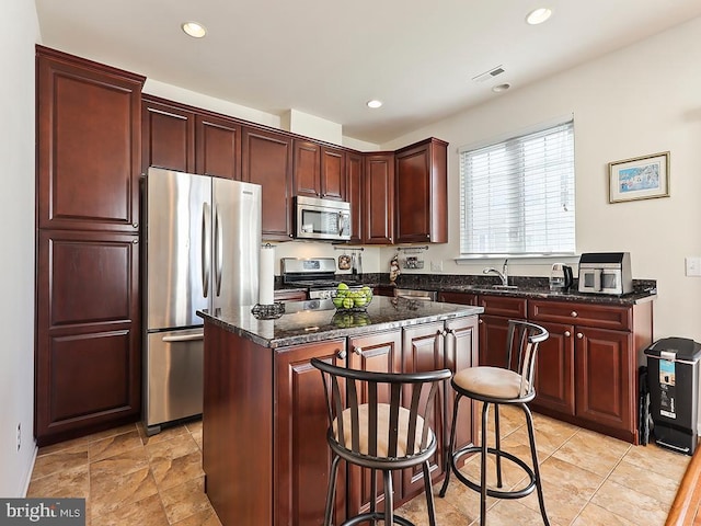 kitchen with visible vents, appliances with stainless steel finishes, a center island, dark stone countertops, and a kitchen bar