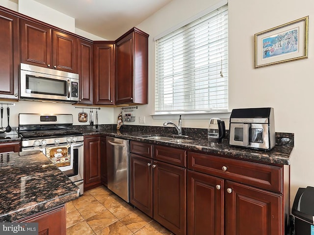 kitchen featuring dark stone counters, appliances with stainless steel finishes, a sink, and reddish brown cabinets