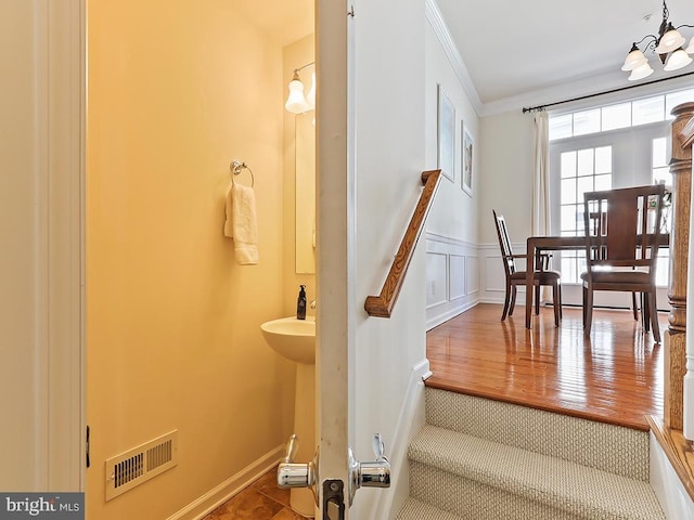 stairway with visible vents, wainscoting, wood finished floors, crown molding, and a decorative wall