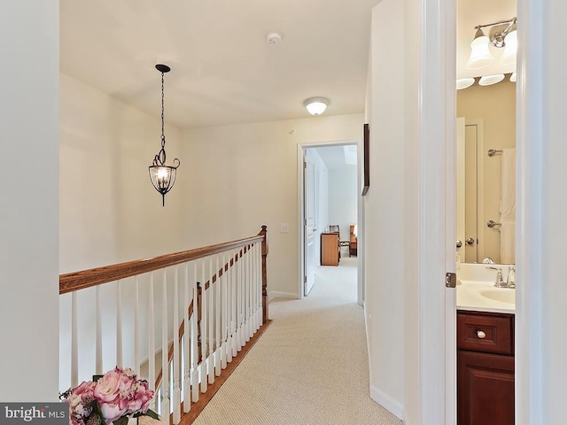 corridor with baseboards, light colored carpet, a sink, and an upstairs landing