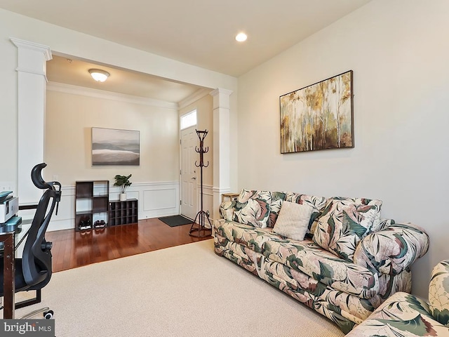 living area featuring a decorative wall, a wainscoted wall, wood finished floors, ornamental molding, and ornate columns