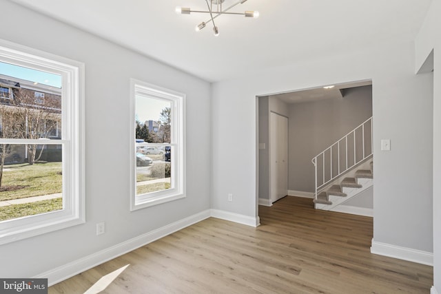 spare room with baseboards, plenty of natural light, stairway, and wood finished floors