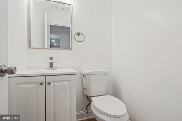 half bathroom with toilet, vanity, visible vents, and baseboards