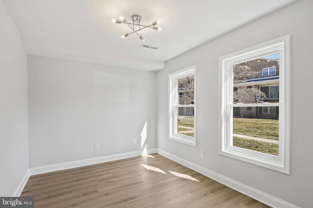 empty room featuring visible vents, a notable chandelier, baseboards, and wood finished floors