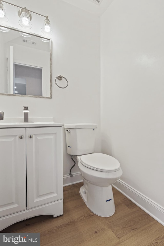 half bath featuring visible vents, toilet, vanity, wood finished floors, and baseboards