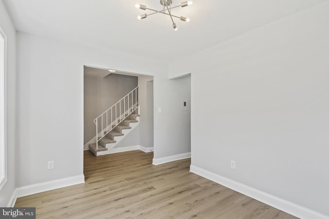 spare room featuring stairs, a notable chandelier, wood finished floors, and baseboards