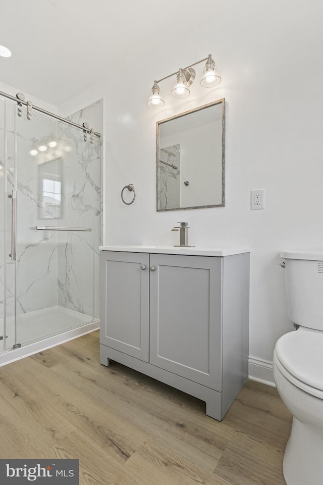 bathroom with toilet, a marble finish shower, wood finished floors, and vanity