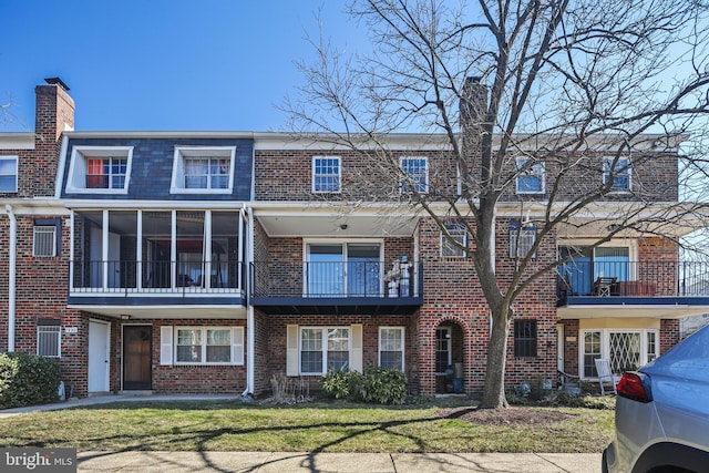 view of front of home featuring a front yard, brick siding, a chimney, and mansard roof