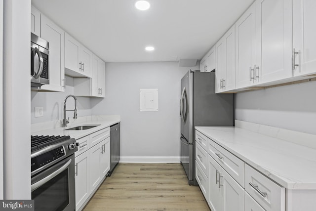 kitchen with stainless steel appliances, a sink, baseboards, white cabinets, and light wood-type flooring