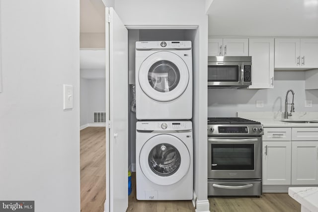 washroom with visible vents, light wood-style floors, stacked washer / dryer, a sink, and laundry area