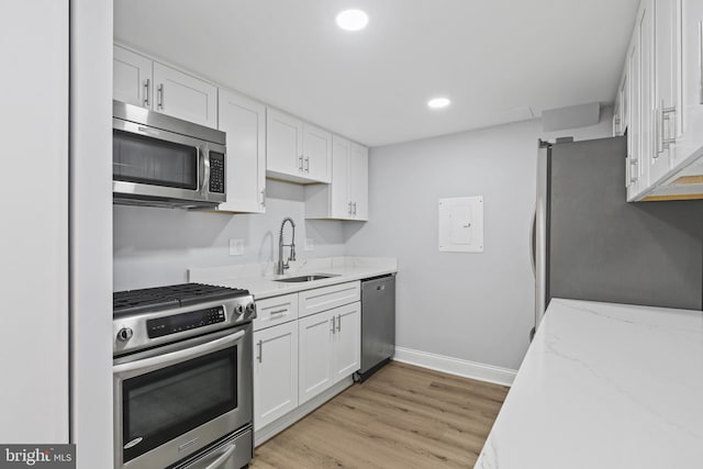 kitchen with appliances with stainless steel finishes, light wood-style floors, white cabinets, and a sink