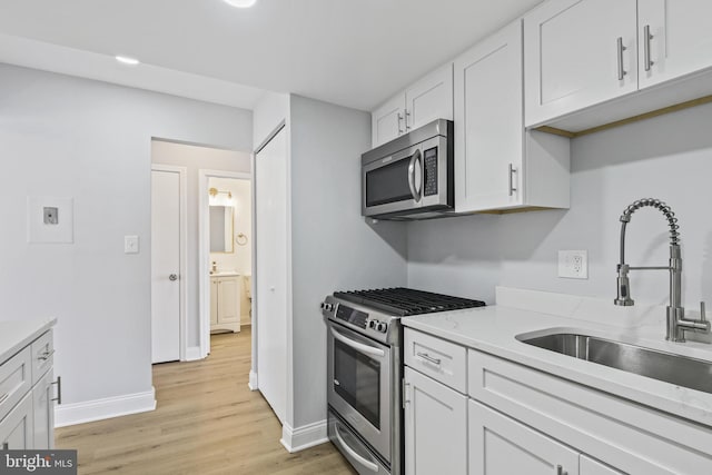 kitchen with a sink, white cabinetry, light countertops, appliances with stainless steel finishes, and light wood-type flooring