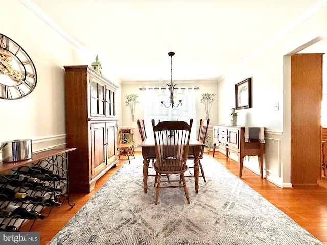 dining room with an inviting chandelier, crown molding, wood finished floors, and a wainscoted wall