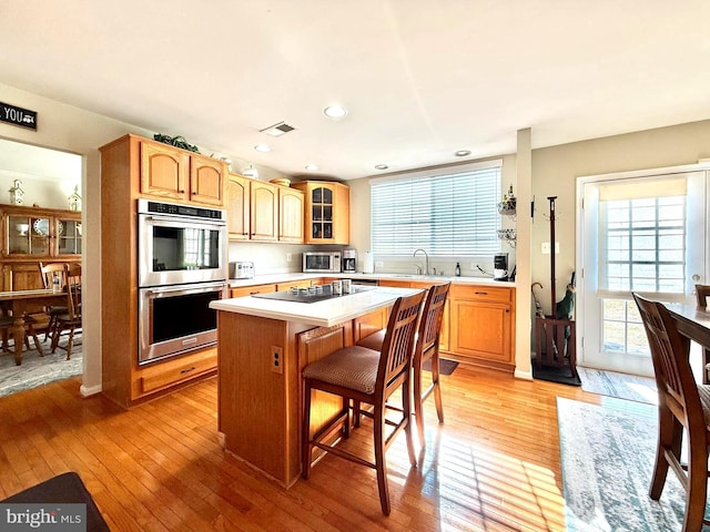 kitchen featuring a sink, a center island, stainless steel appliances, light wood-style floors, and light countertops