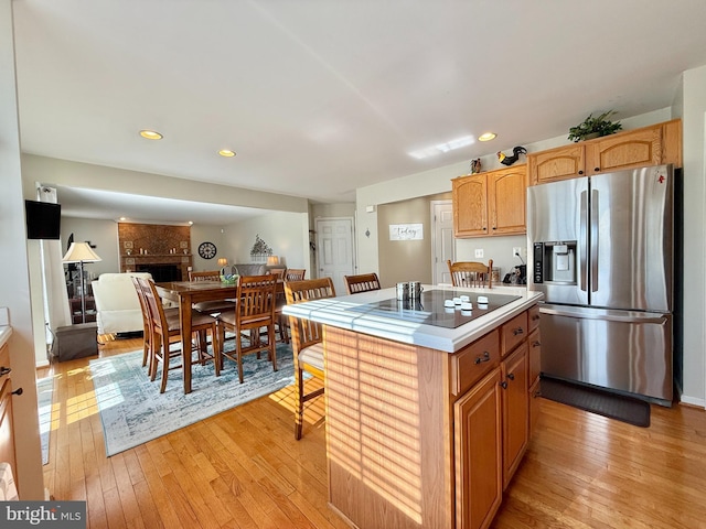 kitchen with a brick fireplace, light wood-style floors, stainless steel fridge, and a kitchen island