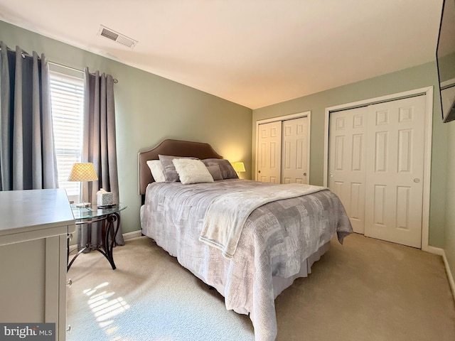 bedroom with light carpet, visible vents, two closets, and baseboards