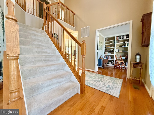 stairs with visible vents, a high ceiling, baseboards, and wood finished floors