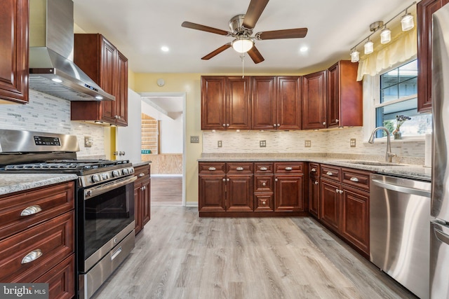 kitchen featuring light wood-type flooring, a sink, light stone counters, appliances with stainless steel finishes, and wall chimney range hood