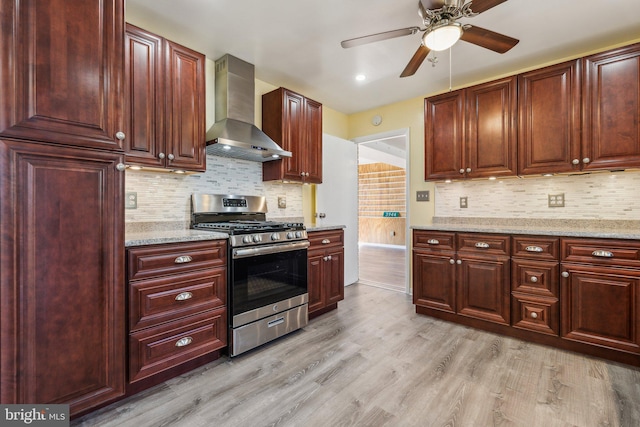 kitchen with light stone counters, dark brown cabinets, light wood-style floors, stainless steel gas range oven, and wall chimney range hood