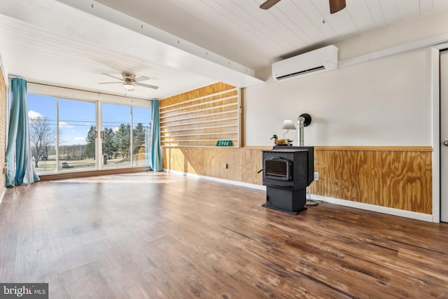 empty room with a wall mounted air conditioner, a ceiling fan, wood finished floors, wooden ceiling, and a wood stove