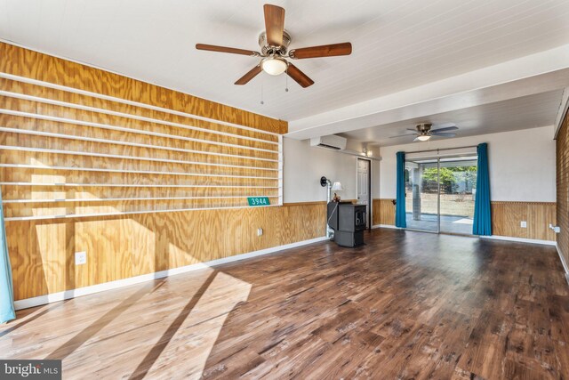 unfurnished living room with wood finished floors, a wood stove, an AC wall unit, wood walls, and wainscoting