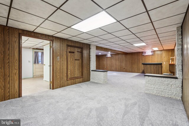 finished below grade area featuring carpet flooring, wood walls, and a drop ceiling